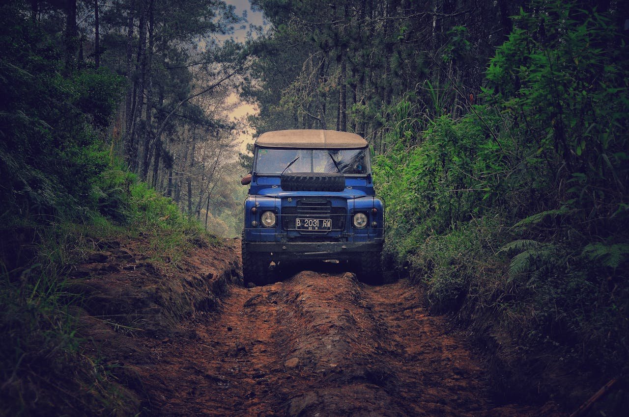 Services-02 Off-road vehicle traversing a rugged dirt path through lush forest in Parongpong, Indonesia.